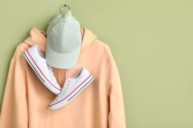 Yeşil arka planda şık şeftali kapüşonlu, şapkalı ve spor ayakkabılı bir askı.