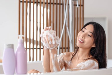 Duş jeli ve banyo lifi şişeleriyle güzel bir Asyalı kadın banyoda banyo yapıyor.
