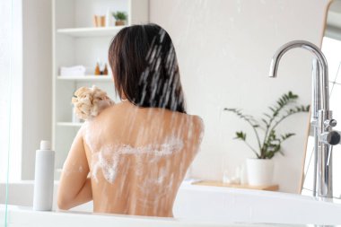 Duş jeli ve banyo lifi şişesiyle güzel bir Asyalı kadın banyo yapıyor.