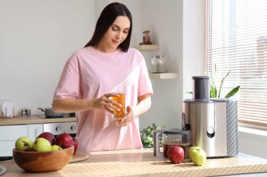 Mutfakta taze elma suyu ve modern meyve sıkacağı olan genç bir kadın.