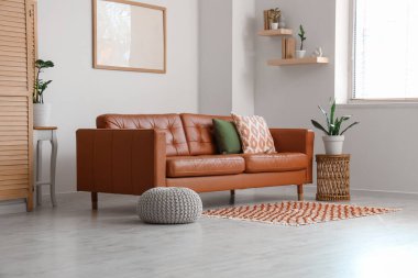 İçinde kahverengi kanepe, boş çerçeve ve bitkiler olan aydınlık oturma odası.