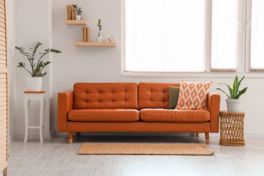 Kahverengi kanepe, raflar ve bitkilerle aydınlık oturma odasının içi