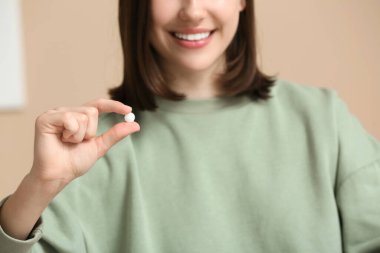 Bej duvarın yanında haplı genç bir kadın, yakın plan.