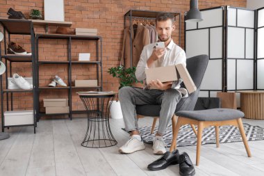 Cep telefonlu genç adam mağazada yeni ayakkabıların fotoğrafını çekiyor.