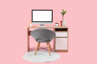 Boş bilgisayar monitörü ve pembe arka planda bitkisi olan modern işyeri