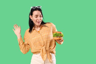 Yeşil arka planda lezzetli burgeri olan güzel genç bir kadın.