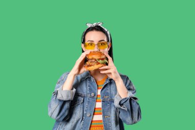 Güzel genç bir kadın yeşil arka planda lezzetli bir burger yiyor.