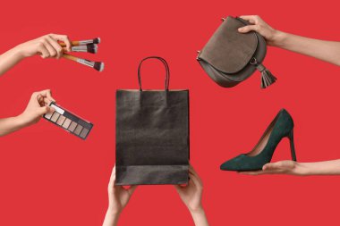 Kozmetik ürünleri, alışveriş çantası ve kırmızı arka planda aksesuarları olan kadın elleri. Kara Cuma İndirimi