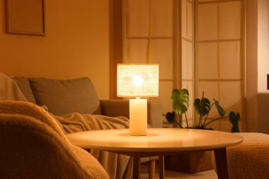 Gece oturma odasının içinde kanepe, katlanan perde ve sehpanın üzerinde parlayan lamba.