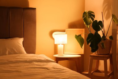 Büyük yataklı, çiçekli, sarı duvarlı, parlak lambalı, gece yatak odasının içinde.