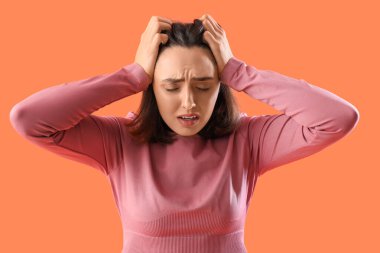 Turuncu arka planda güzel, genç, korkak bir kadın.