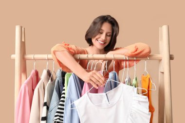 Bej arka planda farklı giysileri olan rafların yanında güzel genç bir kadın.