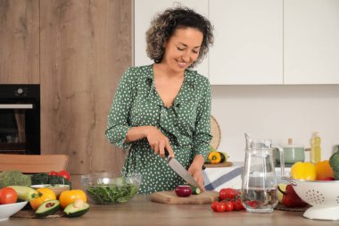 Mutfakta salatalık kesen olgun bir kadın.