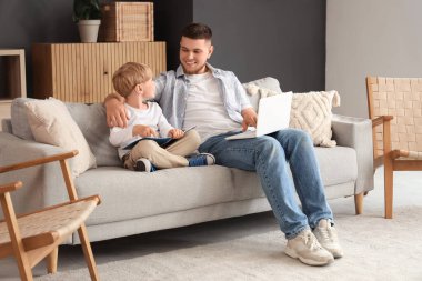 Genç baba evinde dizüstü bilgisayarla oğluna bir şey gösteriyor.