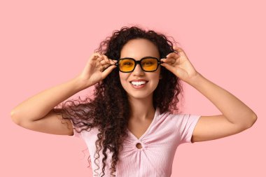 Pembe arka planda güneş gözlüklü mutlu Afro-Amerikan kadın.