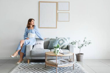 Kanepede oturan genç bir kadın. Evinde boş kareler asıyor.