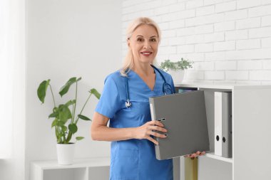 Olgun kadın doktor klinikteki raftan klasör alıyor.