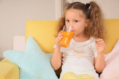 Şirin küçük kız evinde tişörtüne meyve suyu döküyor.