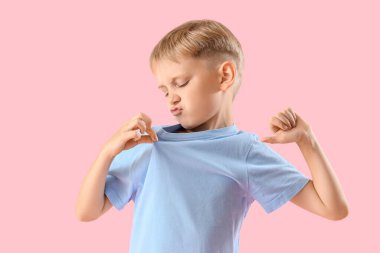 Pembe arka planda iğrenç kokulu tişörtlü çocuk.