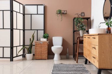 Modern klozet, katlanan ekran ve kahverengi duvarın yanındaki çekmeceler tuvalette.