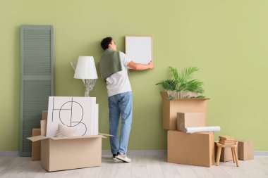 Evdeki yeşil duvara boş bir çerçeve asan genç adam.