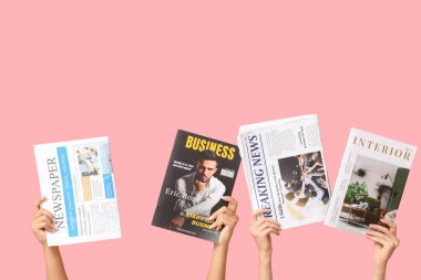 Farklı dergilere ve pembe arka planda gazetelere sahip kadın elleri.