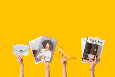 Farklı dergilere sahip kadın elleri, sarı arka planda yüksek topuklu ve şık bir çanta.