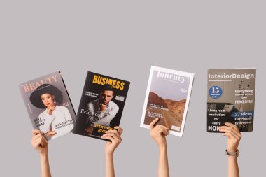 Gri arka planda farklı dergilere sahip kadın elleri