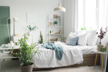 Masalar, raf ünitesi ve bitkilerle aydınlık yatak odasının içinde.