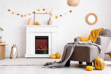 Modern şöminesi, koltuğu, masası ve sonbahar süslemeleri beyaz tuğla duvarın yanında.