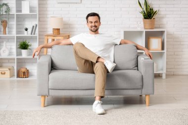Klimalı yakışıklı genç adam oturma odasında kanepede oturuyor.