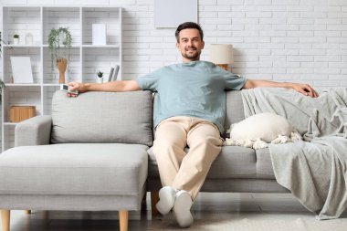 Oturma odasındaki klimalı kanepede dinlenen yakışıklı genç adam.