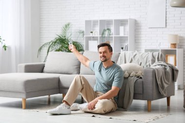 Klimalı uzaktan kumandalı genç adam beyaz tuğla duvarın yanında yerde oturuyor.