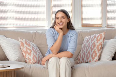 Gülümseyen genç kadın evde koltukta oturan