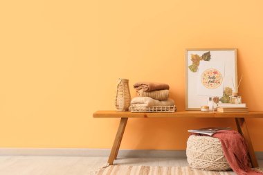 Sonbahar dekorasyonlu şık kıyafetler ve turuncu duvarın yanındaki masada kitaplar.