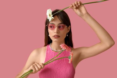 Pembe arka planda Gerbera çiçekleri olan güzel genç bir kadın.