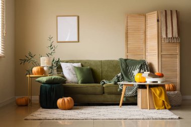 Yeşil kanepeli, masalı ve balkabaklı aydınlık oturma odasının içi.