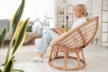 Olgun kadın evdeki yumuşak koltukta dizüstü bilgisayar kullanıyor.