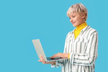 Mavi arka planda dizüstü bilgisayar kullanan olgun bir kadın