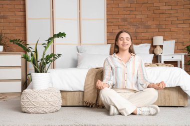 Güzel genç bir kadın, yatak odasında, yatağın yanında meditasyon yapıyor.