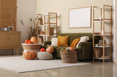 Oturma odasının içinde yeşil kanepe, raflar ve farklı balkabaklarından oluşan hasır sepet var.