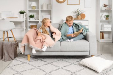 Evdeki kanepede ekose kitap okuyan küçük çocuklar.