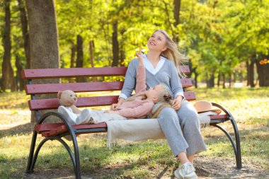 Parkta annesinin oturduğu bankta bir şeye işaret eden sevimli küçük kız.