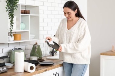 Güzel, genç ve mutlu bir kadın mutfakta kağıt havluyla tabakları siliyor.