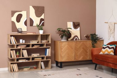 Kitapları, çiçekleri ve kahverengi duvarı olan modern raf ünitesi.