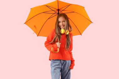 Turuncu şemsiyeli ve pembe arka planda kulaklıkları olan tatlı bir kız.