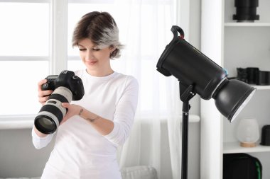 Stüdyoda çalışan profesyonel fotoğraf makinesi ve ışıklandırması olan genç ve güzel bir bayan fotoğrafçı.