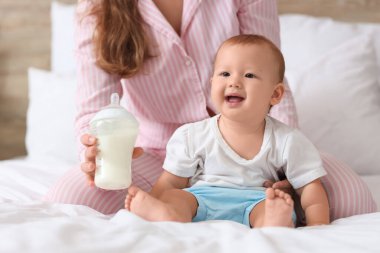 Bir şişe sütü olan genç bir anne ve küçük bebeği yatak odasında.