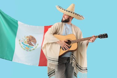 Şapkalı yakışıklı adam mavi arka planda Meksika bayrağıyla gitar çalıyor.