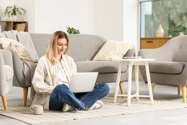 Evde dizüstü bilgisayar kullanan genç bir kadın.